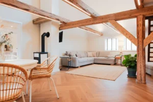 Heller Wohnbereich der Ferienwohnung Anna auf dem Ilsehof: Kaminofen, XXL-Ecksofa, Essbereich mit Korbstühlen und sichtbare Holzbalken