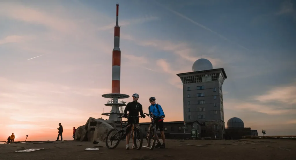 Brocken-Gipfel bei Sonnenuntergang mit Sendemast und Radfahrern.
