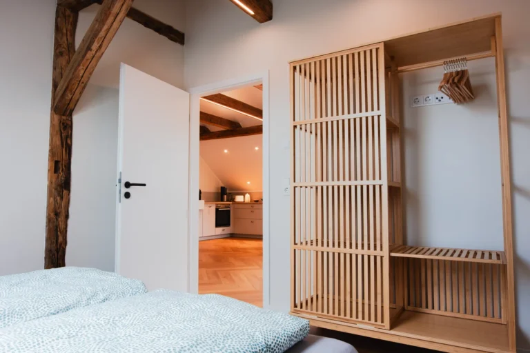 Schlafzimmer der Ferienwohnung Berta auf dem Ilsehof mit Doppelbett, Holzbalken und Blick zur offenen Tür in den Küchenbereich