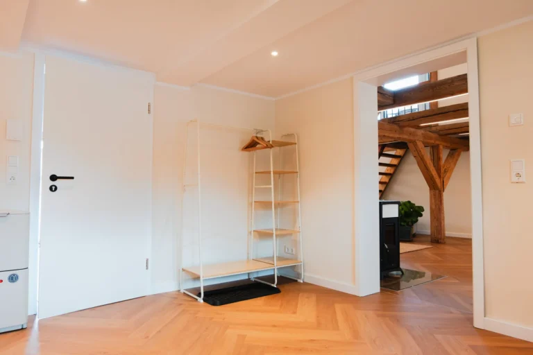 Eingangsbereich der Ferienwohnung Anna auf dem Ilsehof mit offenem Garderobenregal, Holzboden und Blick auf Kaminofen und Galerie