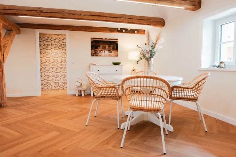 Essbereich der Ferienwohnung Anna auf dem Ilsehof mit rundem Tisch, vier Korbstühlen und sichtbaren Holzbalken