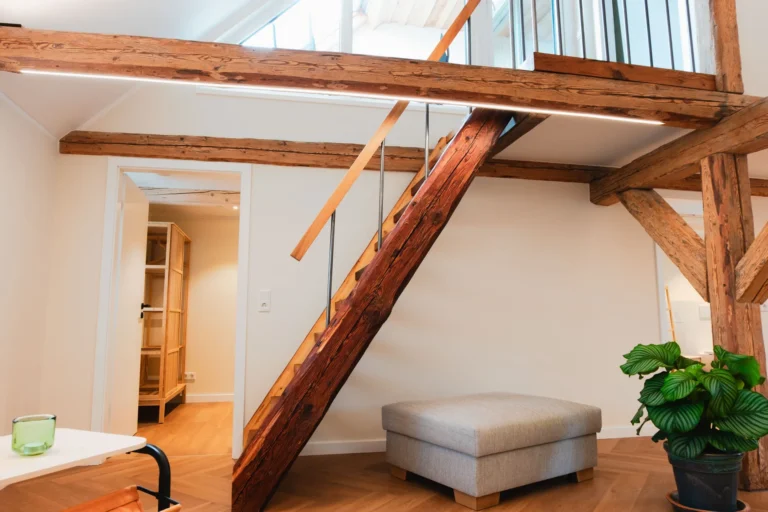 Treppenaufgang zur Galerie in der Ferienwohnung Anna auf dem Ilsehof mit sichtbaren Holzbalken, Hocker und Topfpflanze