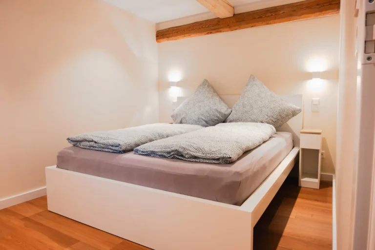Modernes Schlafzimmer der Ferienwohnung Anna auf dem Ilsehof mit Doppelbett, Holzboden, neutralen Farben und sichtbarem Deckenbalken