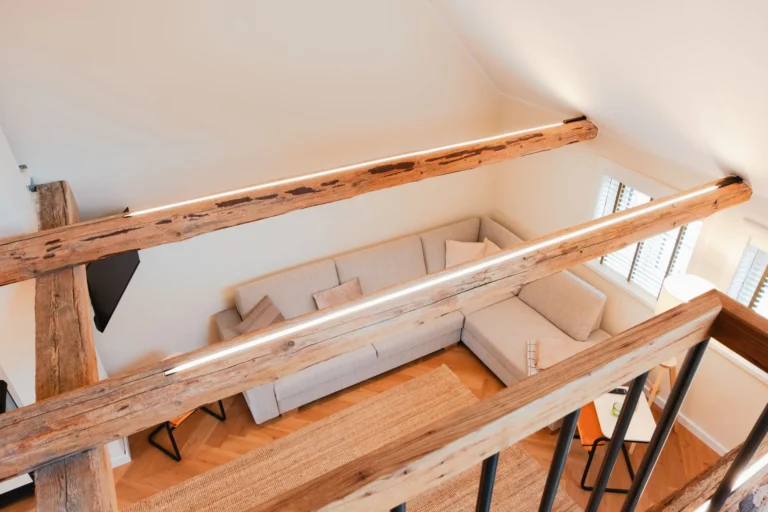 Blick von der Galerie der Ferienwohnung Anna auf den Wohnbereich mit großem Ecksofa, Teppich und sichtbaren Holzbalken