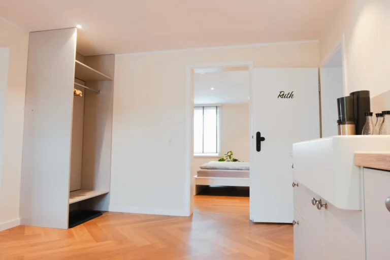 Blick vom Eingangsbereich der Ferienwohnung Ruth in den hellen Wohnraum mit sichtbaren Holzbalken, Treppe ins Obergeschoss und moderner Einrichtung.