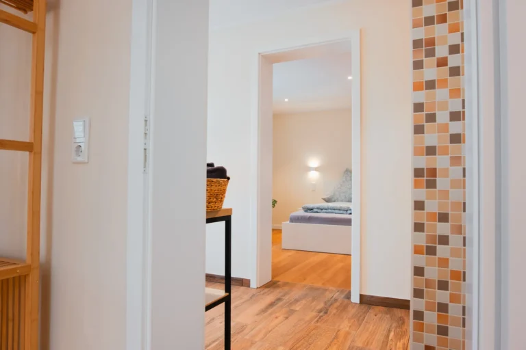 Blick vom einen Schlafzimmer aus, durch das Badezimmer in das andere Schlafzimmer der Ferienwohnung Ruth, im Vordergrund Holzregal mit Handtüchern.