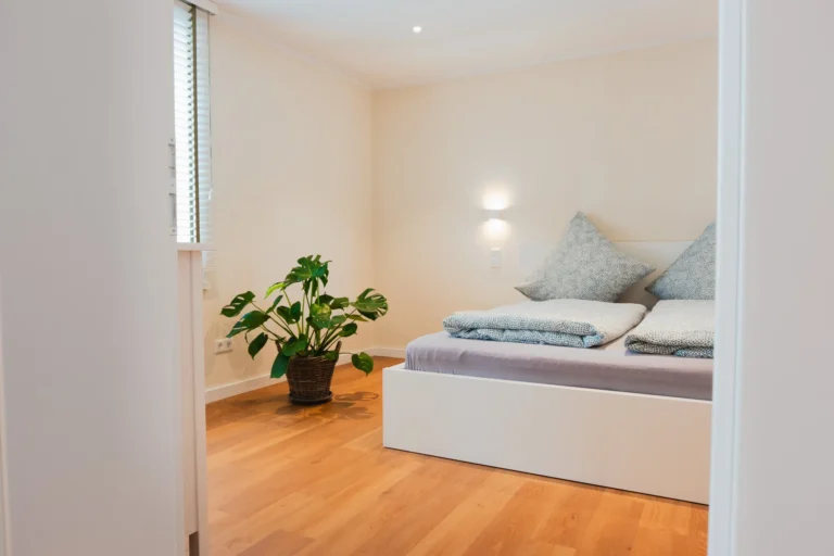 Blick in das Schlafzimmer der Ferienwohnung Ruth mit Doppelbett, Holzboden und einer großen Zimmerpflanze in der Ecke.