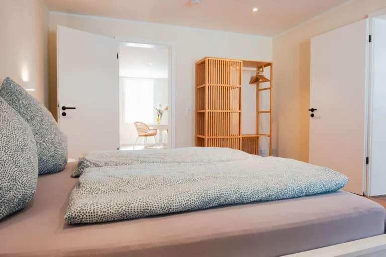 Blick vom Bett in den Essbereich der Ferienwohnung Ruth mit Rattanstühlen und hellen Wänden.