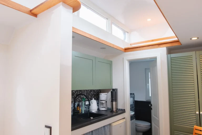 Küchenzeile im Tiny House Mimi mit schwarzen Akzenten und Blick ins Bad