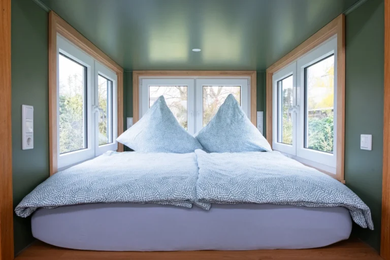 Doppelbett in der Schlafnische des Tiny House Mimi – grüne Wände, Panoramafenster, Ilsehof Harz