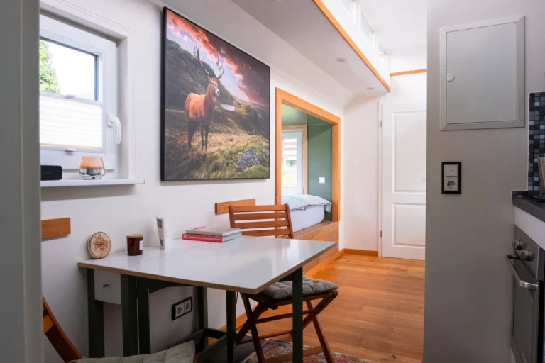 Essbereich mit Holztisch und Hirsch-Kunstdruck im Tiny House Mimi – Ilsehof Ferienunterkunft Harz